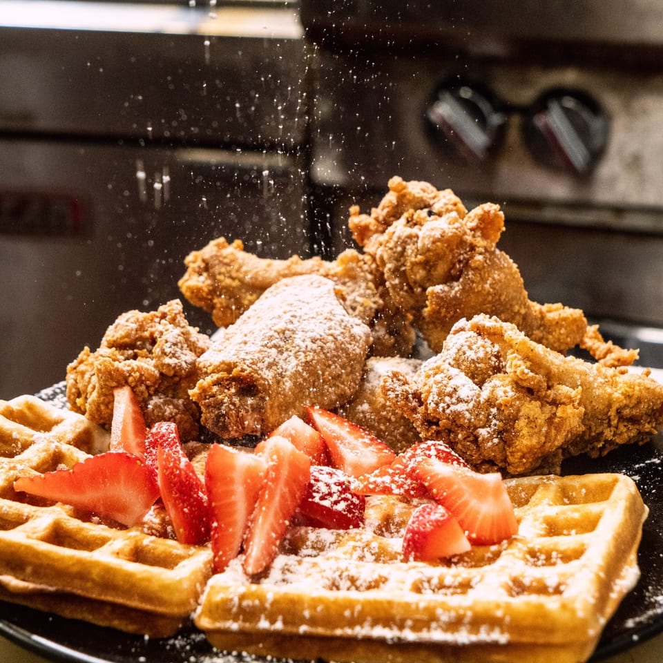 Crispy fried chicken and waffles with strawberries, dusted with powdered sugar at Butter Funk Kitchen.