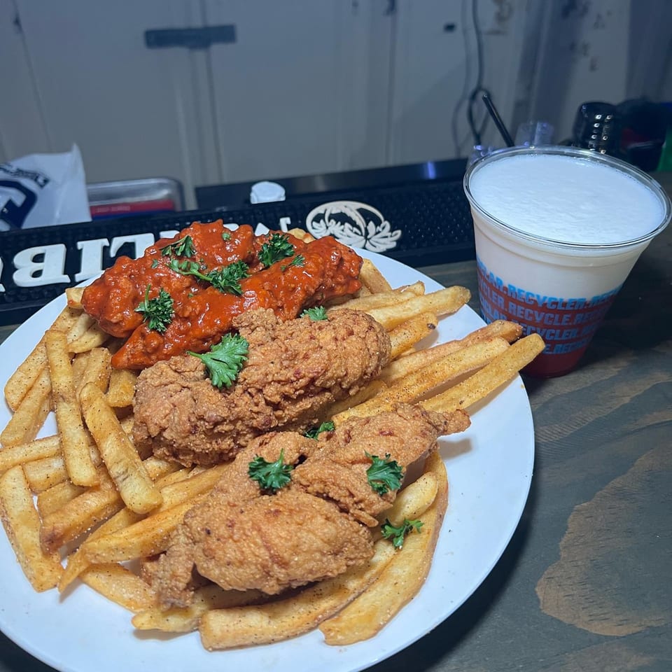 A plate of Butter Funk Kitchen's soul-food chicken tenders, fries, and a drink on a bar.