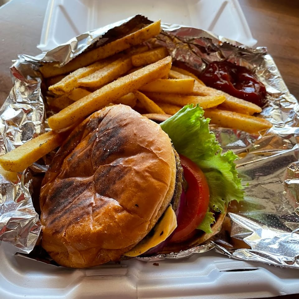 A Butter Funk Kitchen cheeseburger with lettuce and tomato, alongside seasoned fries and ketchup in a takeout container.