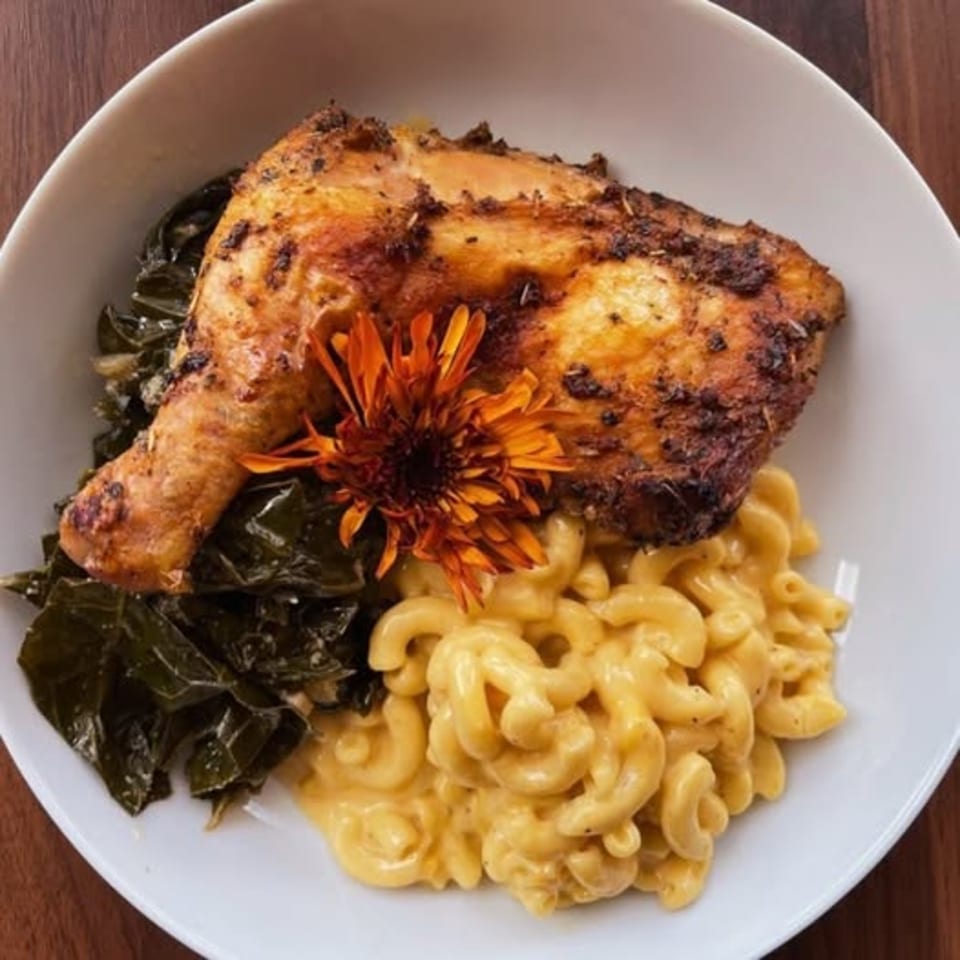 A soul-food plate with a roasted chicken leg, collard greens, and creamy macaroni and cheese.
