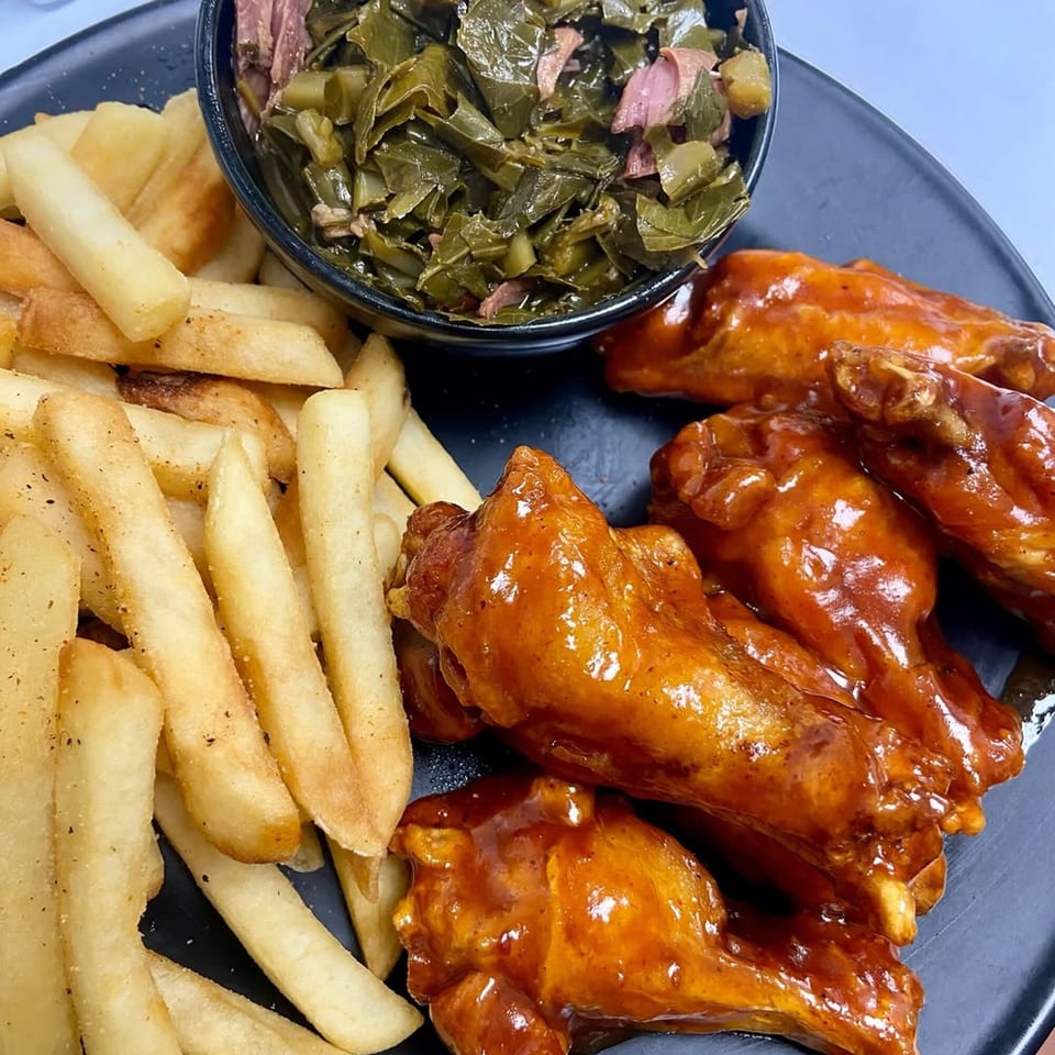 Soul food plate with golden french fries, BBQ chicken wings, and a bowl of collard greens.